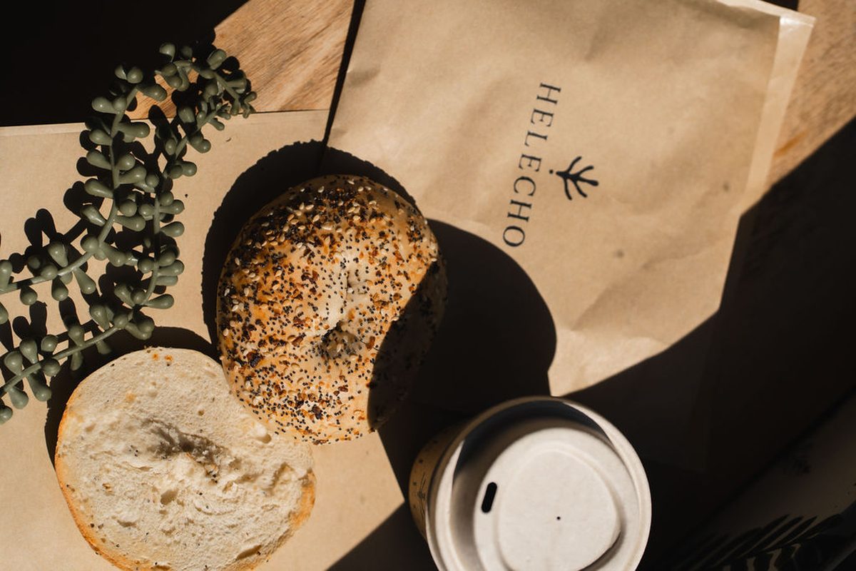 An everything bagel with cream cheese beside a Helecho bag